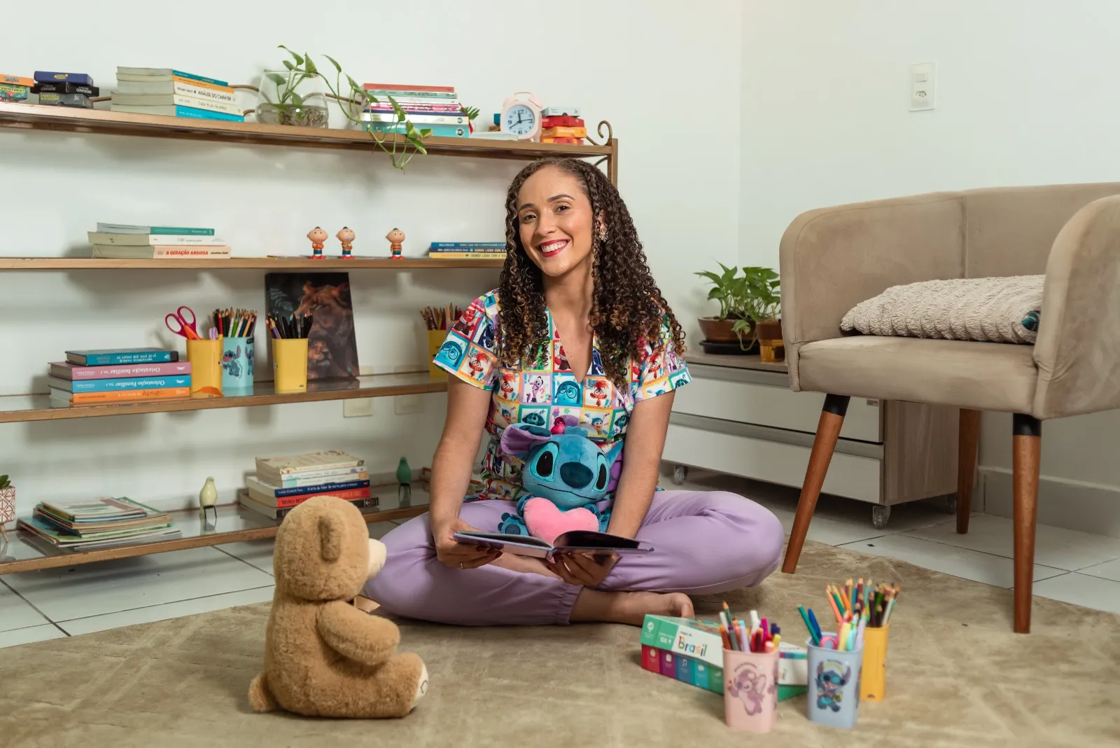 Consultório acolhedor com poltronas, estante de livros e a psicóloga sentada no tapete
