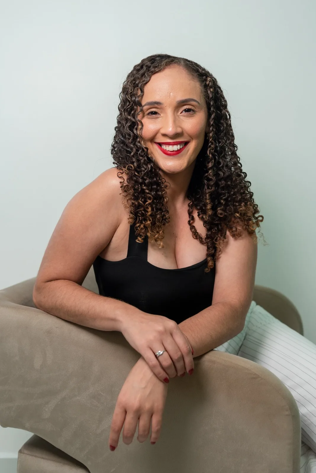 Milena Santos sorrindo para a câmera, apoiada no braço de uma poltrona bege